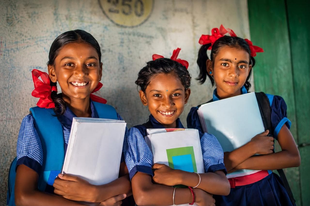 Schoolgirls in uniform holding books and smiling — education.